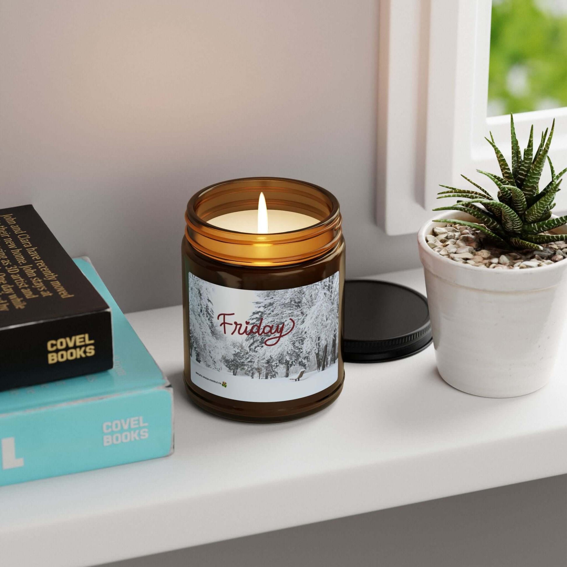 Friday Vibes Scented Soy Candle on a shelf with a warm glow next to books and a small potted plant.